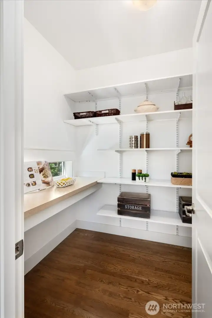 Spacious walk-in pantry offers abundant shelving, exceptional storage, and a built-in workspace, all beautifully illuminated by natural light for effortless organization.