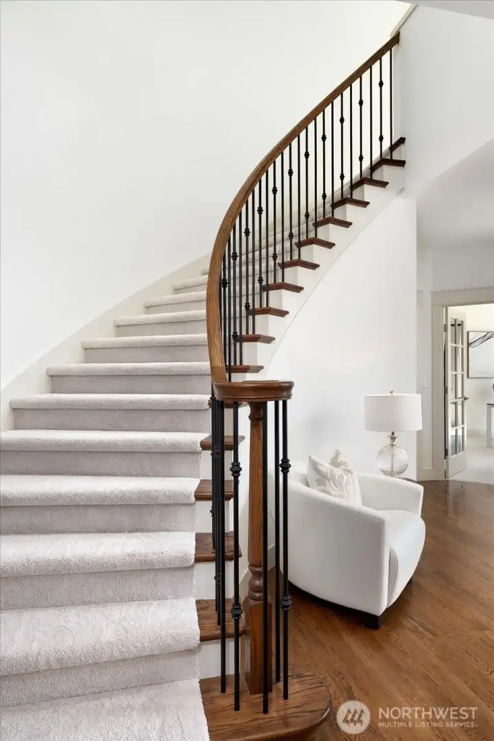 The graceful curved staircase is a striking architectural centerpiece, featuring rich hardwood railings, elegant iron balusters, and luxurious new carpeting as it leads to the private second level, where all four bedrooms are thoughtfully situated.