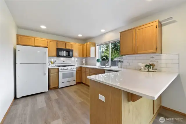 The stylish kitchen is a showstopper, featuring all new quartz countertops, a farm sink, Kohl faucet and ceramic tile backsplash that adds a touch of modern sophistication. A bar seating area invites casual dining, while the pantry provides ample storage. The freshly stained solid wood cabinets bring warmth and character, complemented by new beautiful laminate flooring. Recessed can lights create a bright, functional space—ideal for culinary creativity and gatherings alike.