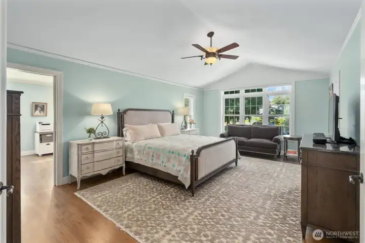 The spacious primary suite features vaulted ceilings, white Oak hardwood floors, ceiling fan, and a sitting room/office/exercise room.