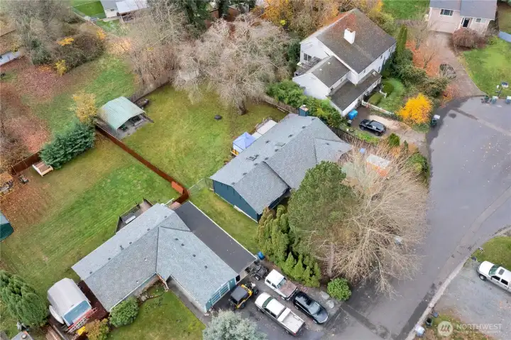 Aerial view of the front left of the property depicting the mature shrubs and trees out front plus the large yard with the car port can be seen.