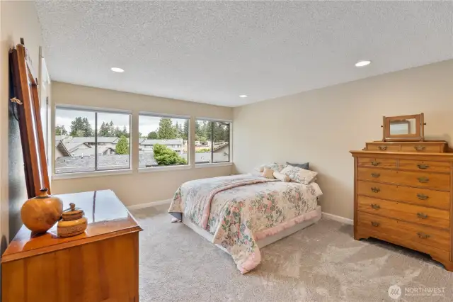 Spacious primary bedroom with lots of windows and recessed lighting.