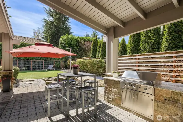 A true extension of the home—covered outdoor living with built-in grilling, dining, and lounge spaces, set against a private, thoughtfully landscaped backdrop.