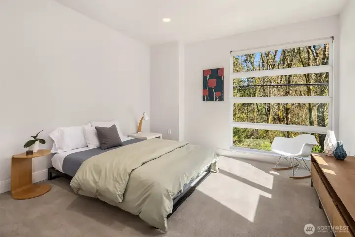 Light-filled secondary bedroom with expansive windows and a tranquil, tree-lined outlook.