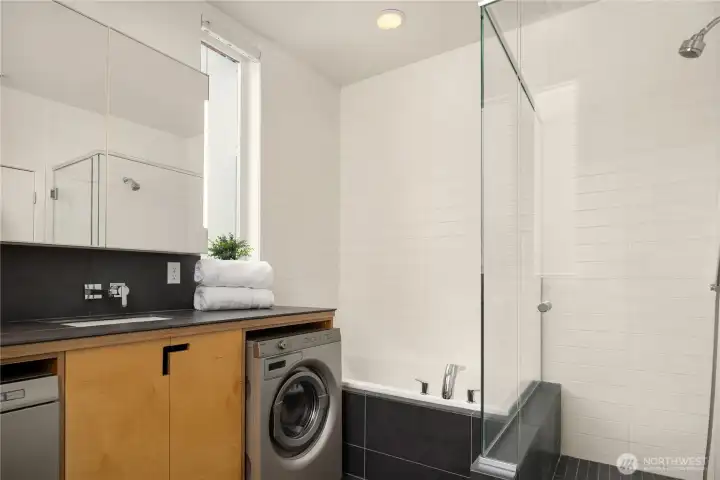 The sleek bathroom combines modern style with everyday convenience, featuring a soaking tub/shower combo, porcelain tile vanity and in-unit laundry.