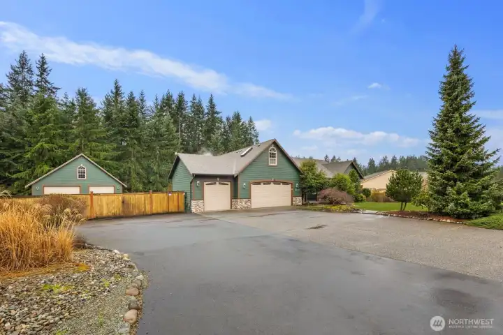 Stanwood home set on just over an acre with a wide driveway approach, attached garage, and a separate detached shop building on the property, surrounded by mature evergreen trees.