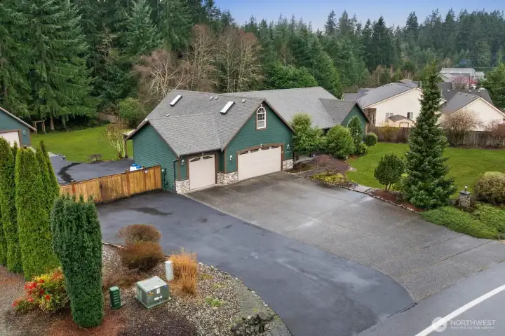 Angled view of the home highlighting the expansive driveway, attached garage, and gated access leading toward the detached shop behind the property.