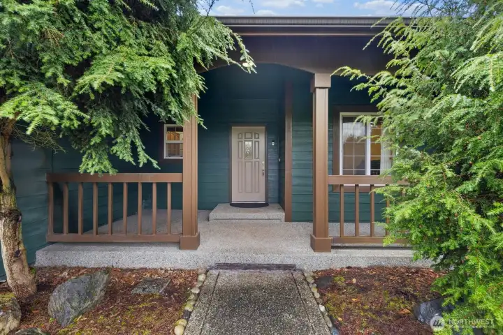 Covered front porch framed by mature landscaping, creating a welcoming entry and sheltered space before stepping inside the home.
