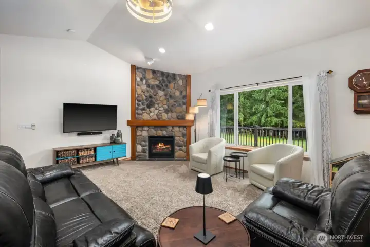 Main living room featuring vaulted ceilings, a stone fireplace, and large windows that bring natural light into the central gathering space.