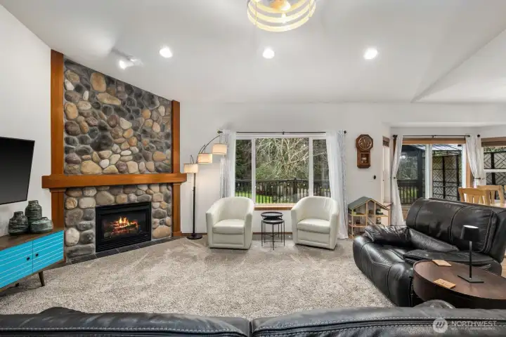 Open living room with a floor-to-ceiling stone fireplace and large picture window that frames views of the surrounding trees and backyard.