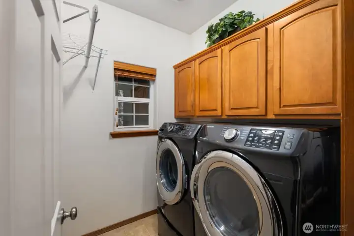 Dedicated laundry room with side-by-side washer and dryer, overhead cabinetry for storage, and a window for natural light.