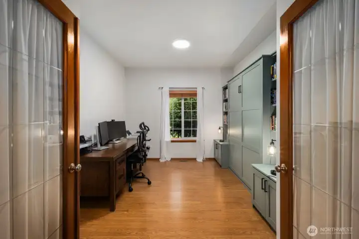 Versatile main-level den with murphy bed, double glass doors and a window overlooking the property, offering space for a home office, study, or creative workspace.