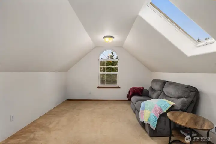 Additional view of the upper-level living space highlighting the open layout, skylight, and natural light from the arched window.