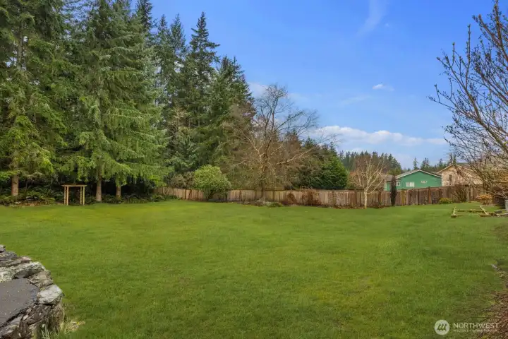 Expansive backyard with a wide open lawn bordered by mature trees and fencing, providing a private outdoor setting with room for recreation and gardening.