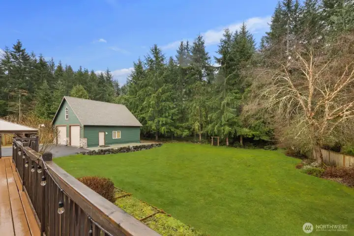 Raised deck perspective showcasing the open lawn, mature trees, and outbuilding beyond.