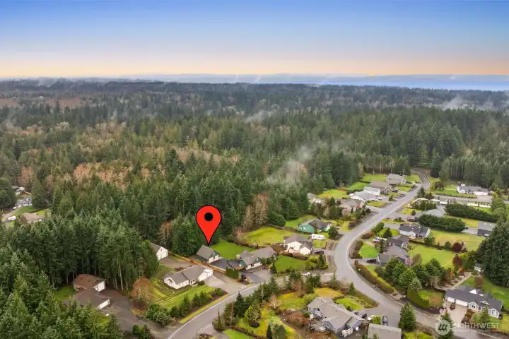 Elevated drone view looking across the surrounding wooded landscape toward the distant water and surrounding communities.