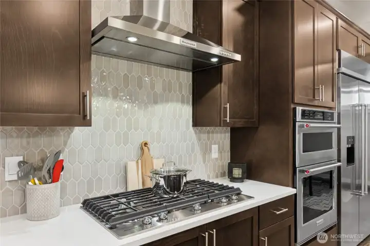 Gourmet kitchen with gas cooktop, separate hood, in-wall oven and microwave.  Gourmet kitchen with large center island, quartz counters, loads of cabinets, built-in 48" fridge and in-wall oven & microwave next to your large family room. Materials, colors, and finishes will vary. See site agent for details.