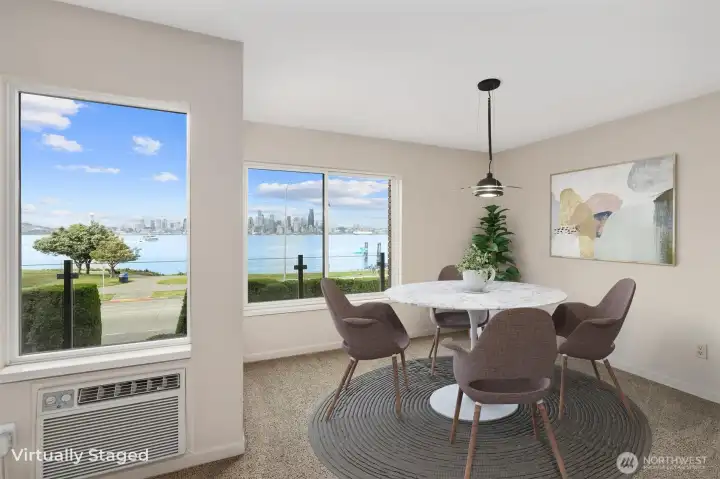 The dining area is perfectly positioned to take full advantage of the stunning city skyline and Puget Sound views, creating an inviting space to gather with friends and enjoy memorable meals together. Large windows bring in abundant natural light while showcasing the breathtaking scenery beyond. Also note the convenient A/C unit located to the left in the photo, providing added comfort during warmer summer days.