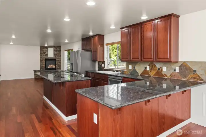 Kitchen with granite tile countertops. Family room with fireplace in the background.