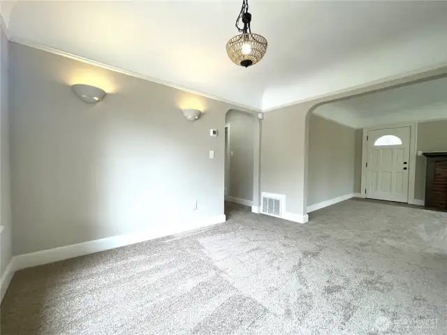 Standing in the corner of the dining room and looking towards the hallway and front door. Features the arched doorways. Updated lighting to keep things modern.  Note the coved ceilings and the crown molding here. Beautiful!