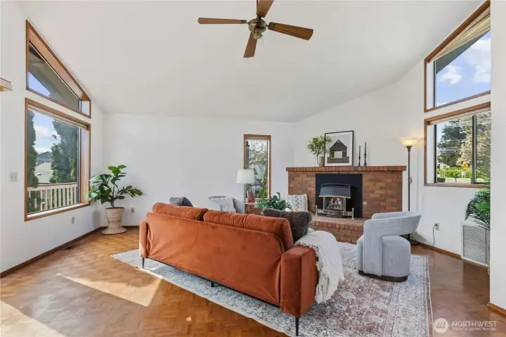 The living room is surrounded by windows but anchored by a cozy brick fireplace.