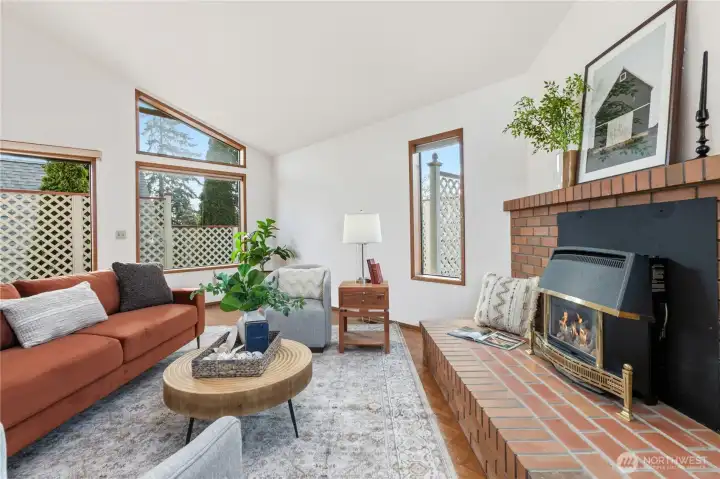 Living room with vaulted ceilings, exposed beam, and brick fireplace, creating a spacious setting with a warm focal point.