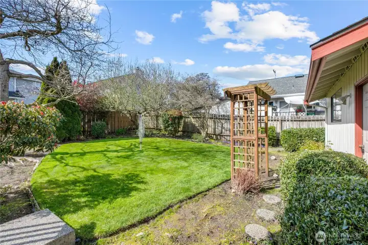 Fully fenced backyard with lawn, mature landscaping, and garden space.