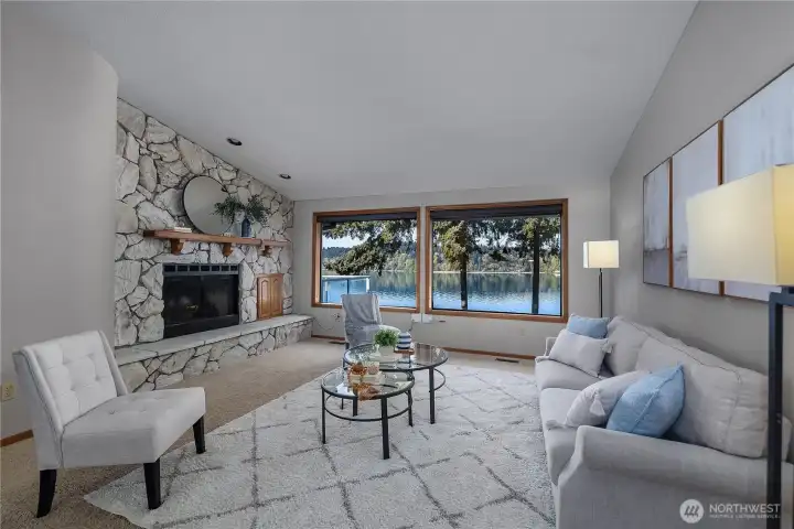 Main living room framed by stunning water views and a dramatic stone fireplace.