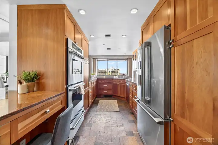 Natural wood cabinets, desk work station, stainless steel appliances, and slate floors in this built kitchen.