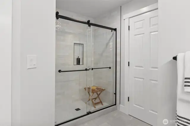 Primary bathroom shower with brand new floor to ceiling tile, fixtures and glass doors