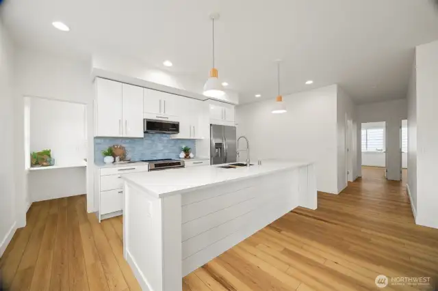 Looking across the island toward the kitchen with the walk-in butler's pantry to the left and the wide hallway to bedrooms and full bathrooms to the right.