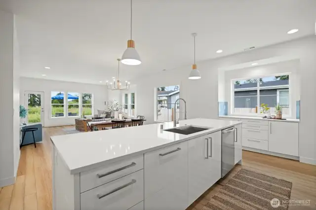 Looking across the large island with the eating bar and deep sink toward the dining area and living room. There is a lovely coffee or prep area below the window to the right of the island.
