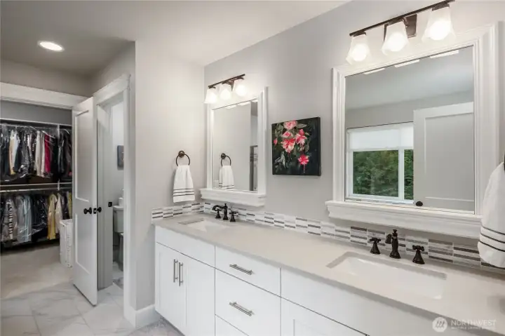 Primary bathroom has quartz countertops and double undermount sinks with custom tile backsplash. Showing private water closet and walk-in closet.