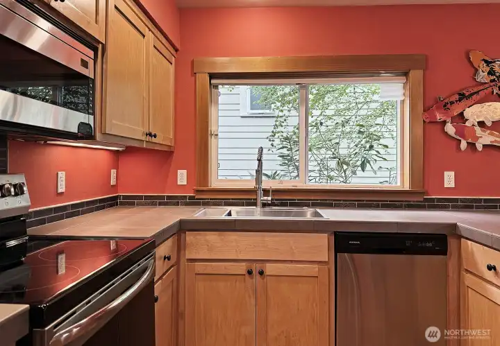 Maple cabinets with tile counter tops and stainless steel appliances.