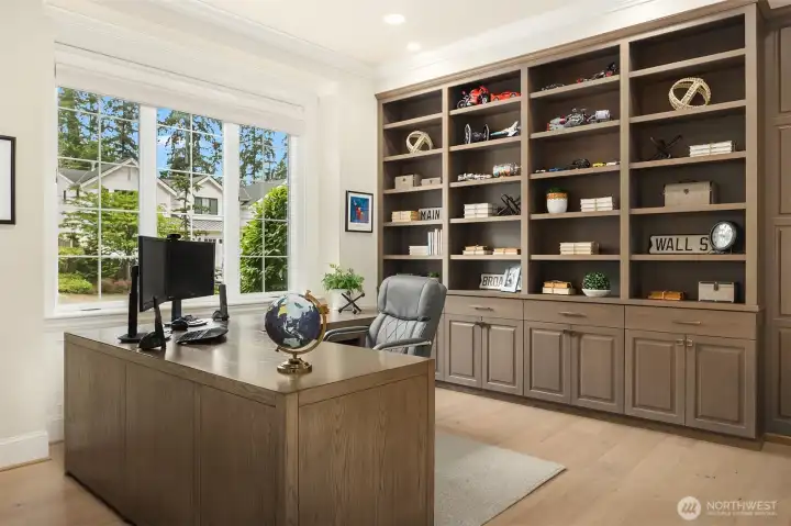 Main floor office with custom library shelving in a warm elegant wood. Large picture window to the front yard with remote operated blinds for privacy when needed.