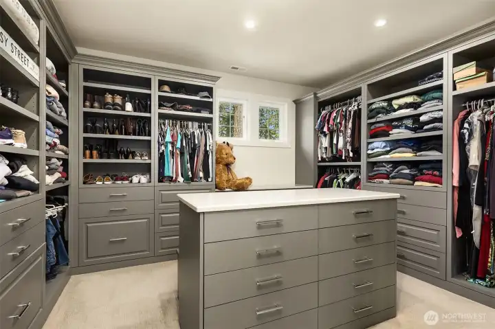 Dream walk-in closet with custom cabinetry, island dresser, & seating behind. Full-size lighted mirror & windows for natural light, too!