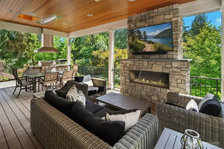 Cozy fireplace & mounted flat screen TV. Beyond is a grilling station + Ooni gas pizza oven.