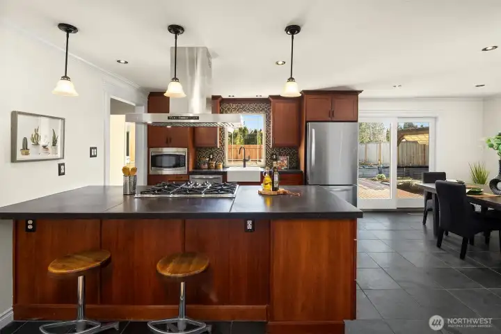 Slab countertops offer both an abundance of prep space, but also space where family and guests can hang out and chat. Industrial style five burner stove and overhead extraction fan is a standout modern feature.