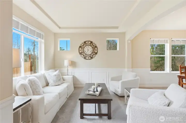 Formal living room with wainscoting, tray ceiling, and tree-lined views