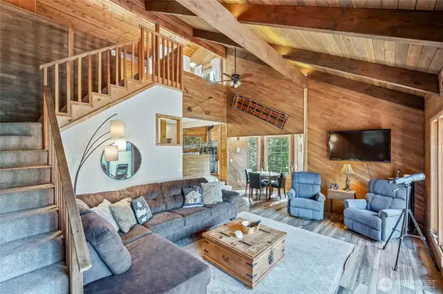 Bright great room with vaulted wood ceilings and a cozy wood stove fireplace.