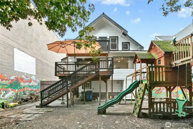 The fully-fenced backyard has a play structure, shady Japanese red oak trees, murals including a movie screen, and a large deck.
