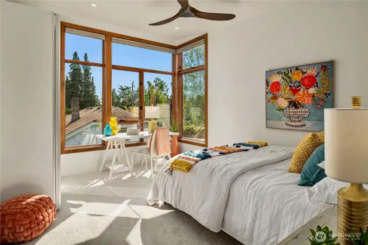 A bright second bedroom with oversized windows and a versatile layout ideal for work or rest.