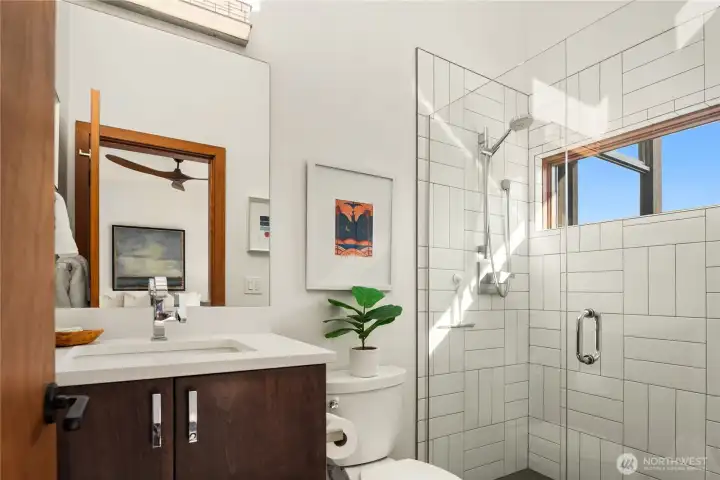 Sleek white tile and a glass shower create a crisp, modern en suite feel.