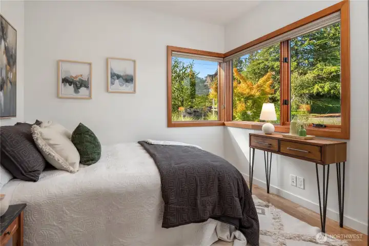 Main level bedroom with wide windows overlooking lush landscaping and fall color.