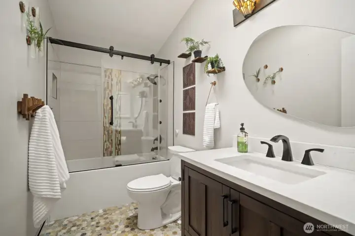 Fully remodeled upper bath showcasing custom tile, tub/shower, frameless glass shower door, and modern hands-free flush toilet.