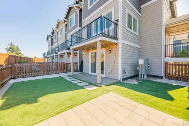 Fully fenced backyard features turf, paver patio and white rock