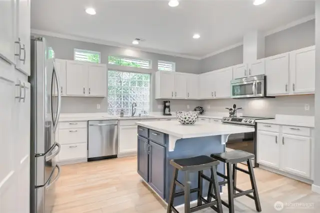Spacious kitchen with white cabinets, blue island, stainless steel appliances, lots of cabinets & counter space