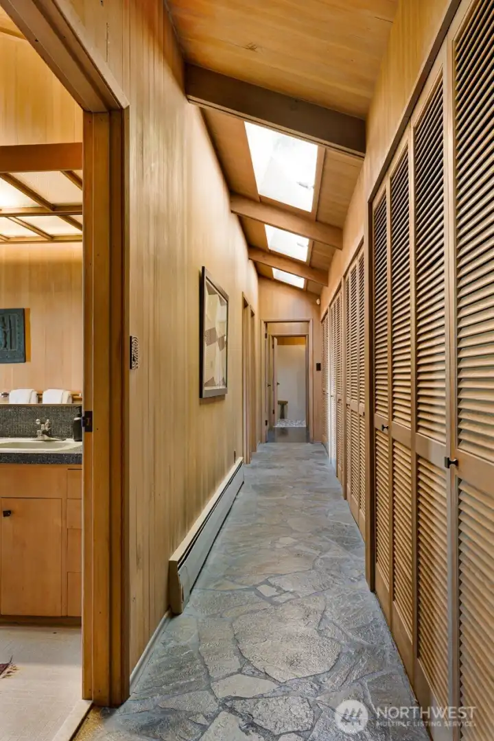 The bedroom wing, hallway continues the stone floors and a course of skylights and closets the entire length, past the two secondary bedrooms and down to the en-suite primary. The bedroom wing, hallway continues the stone floors and a course of skylights and closets the entire length, past the two secondary bedrooms and down to the en-suite primary.
