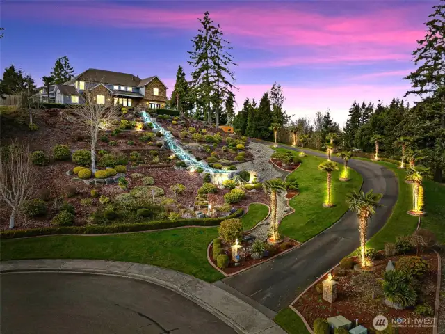 Welcome to your private paradise! As you ascend the hill, a gracefully curved driveway lined with majestic palm trees leads you to your own secluded oasis. The meticulously designed landscaping is a true work of art, featuring an elegant arbor, sculpted concrete borders, and strategically placed rocks that add both charm and structure. Lush greenery, thoughtfully arranged bushes, and towering trees create a sense of privacy, while beautifully crafted retaining walls enhance the natural beauty of the space.    At the heart of it all, a breathtaking waterfall cascades, filling the air with the soothing sounds of flowing water and infusing the surroundings with tranquility. The towering palms add to the serene ambiance, making this retreat an inviting, picture-perfect haven. Whether you're unwinding in solitude or entertaining guests, this stunning setting is sure to leave a lasting impression.