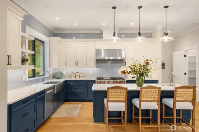 Blue Shaker cabinetry with sleek black door pulls, Quartz countertops, hand crafted Spanish tile backsplash, under cabinet lighting, Full wall ceramic tiled backsplash, Expansive kitchen island with undermount vegetable sink, room to seat 6, Stainless steel 48” six-burner Wolf range with stainless hood & dual ovens, 48” Sub-Zero Double Column refrigerator, Bosch dishwasher, GE Profile microwave built into island
